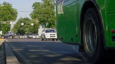 cars, buses and scooters are passing by in city street covered with green trees at sunny summer day in Bishkek, Kyrgyzstan - June