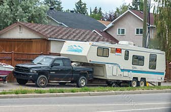 A black pickup truck tows a fifth-wheel RV with a \"FOR SALE\" sign, parked roadside in a