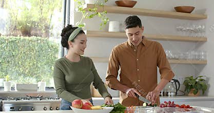 Couple preparing fresh salad at kitchen island chopping cucumber and carrots, sharing smiles