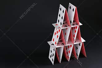 House of playing cards on black background, space for text