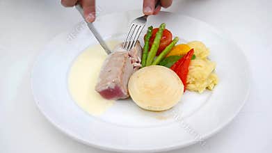 A person eating tuna steak as main dish.