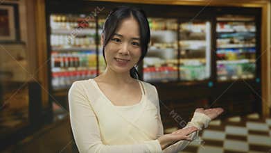 Woman smiling indoors at restaurant pointing towards shelves with beverages highlighting refreshment variety