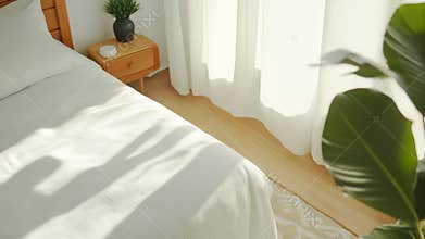 A bright and airy bedroom with a neatly made bed, soft white bedding, and sunlight streaming through sheer curtains