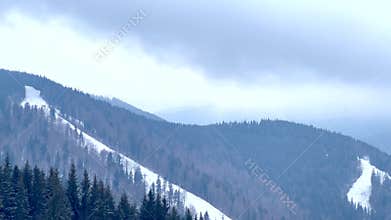 Clouds moving over snowy mountain ski slopes and pine trees