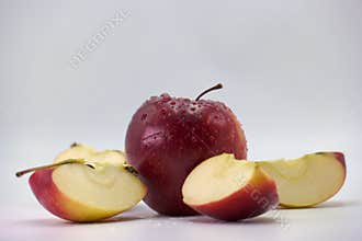 Fresh red apple resting among sliced pieces with dew droplets in a minimalistic background