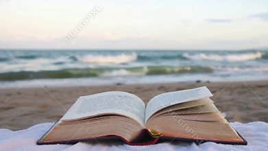 A Serene Beach Scene with a Book Lying Open on a Towel, Waves Crashing Softly in the Background