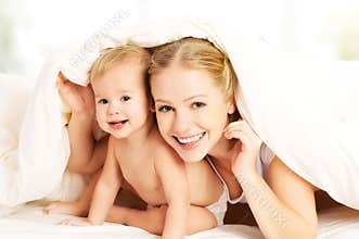 Happy family mother and baby under blankets in bed