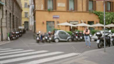 Blurred street scene in rome with defocused people crossing near scooters and historic architecture under umbrellas