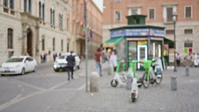 Blurred street view in rome with people walking, vehicles passing by, and defocused scooters near a newsstand in the historic old