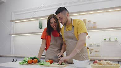 A joyful couple cooks a nutritious meal in their stylish kitchen, wearing matching aprons that enhance their bond and