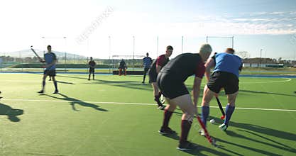 Playing field hockey, men competing in intense match on outdoor field