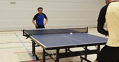 Playing table tennis, two men competing in indoor sports facility