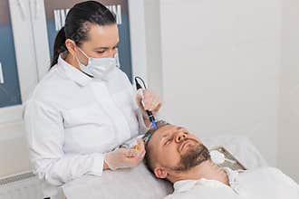 Trichologist doing man improve hair growth procedure, dermapen microneedling, vitamin injections
