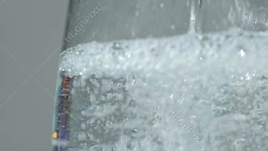 White distilled vinegar is poured into glass bowl macro slow motion. Lots of bubbles in the liquid