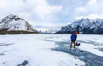 Boy enjoying ice hockey on frozen Lake Minnewanka in the beautiful winter at Banff National Park