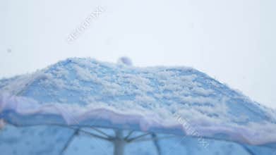 Snow accumulates on a blue umbrella during winter weather