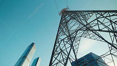 Tower with power transmission lines against office buildings under clear sky