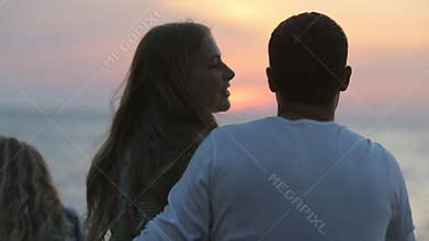 Family sitting near the sea at sunset, the husband