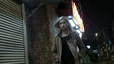 Beautiful blond woman in coat walking alone outdoors at night. Grain. Slow motion.