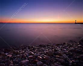 Sunset view over the water near La Rochelle with stones on the shore and a lighthouse in the distance