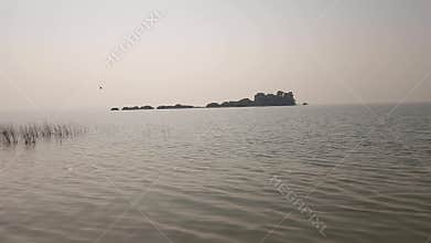 Calm lake water with gentle ripples and distant island under soft natural light