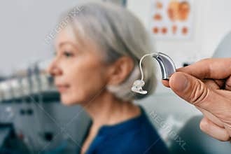 A hearing aid near senior patient's ear at audiology clinic. Hearing solutions, hearing BTE aids