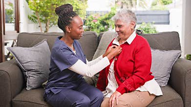 Black Carer Assists Senior Woman with Her Cardigan During a Comforting Home Visit