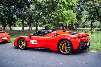 Red Ferrari SF90 stradale Plug-in Hybrid Electric Vehicle PHEV hypercar parked on the garden with asphalt pavement
