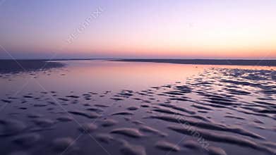 Breathtaking aerial drone view over wide sandy mudflat beach at beautiful purple sunset twilight horizon sky, nature concept