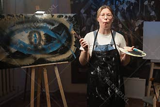 A creative, modern, and successful artist stands looking at the camera and shows off a funny fish-face carving with her lips.
