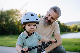 Father helping toddler son learn to ride balance bike for the first time.