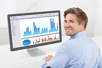 Happy businessman analyzing financial graphs on computer