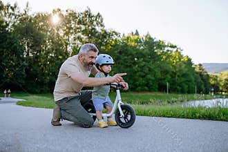Father teaching toddler son to ride balance bike while wearing safety helmet.