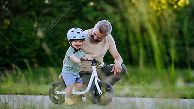 Father teaching toddler son to ride balance bike while wearing safety helmet.