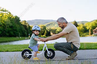 Father helping toddler son learn to ride balance bike for the first time.