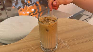 Iced Latte with Milk Coffee and Ice Stirred Through Clear Straw in Glass at Cafe