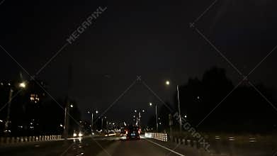 Night traffic on wet city road with car ahead, streetlights, dark sky