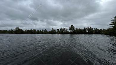 Wide rippling lake beneath heavy gray clouds with distant tree line and