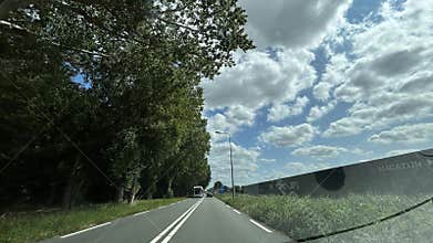 Two-lane country road lined with tall trees under cloudy sky Amsterdam