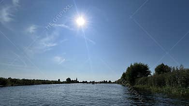 Bright summer river landscape with sparkling water, tall reeds, green shoreline