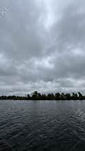 Dramatic overcast sky above calm dark water with distant tree line and