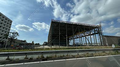 Large modern construction hall beside roadway with steel framework, partly