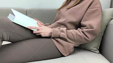 Woman opens book with hands while sitting on sofa at