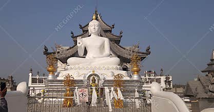 Front view of a large white Buddha statue at an ornate temple under clear blue sky.