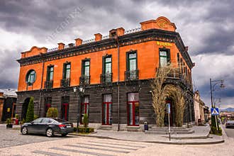 Classic corner building in European town, cloudy weather, parked car, bare tree