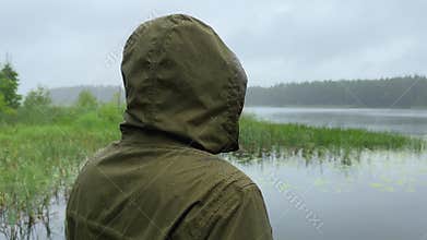 Side profile of a hooded man looking over a lake