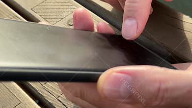 Male hands typing message on smartphone outdoor while sitting at