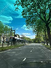 Tree lined urban street with tram stop, empty asphalt lanes, red traffic