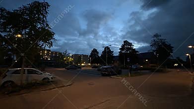 Evening urban street with illuminated office building and parked cars under