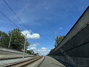 Curving tram tracks beside roadside barrier under bright blue sky with overhead